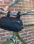 Crossbody Bag in schwarz am Fahrradlenker von grünem Fahrrad vor Mauer