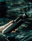 Hand hält DOPPER Insulated Steel – Blazing Black Trickflasche beim Schwimmen im Wasser