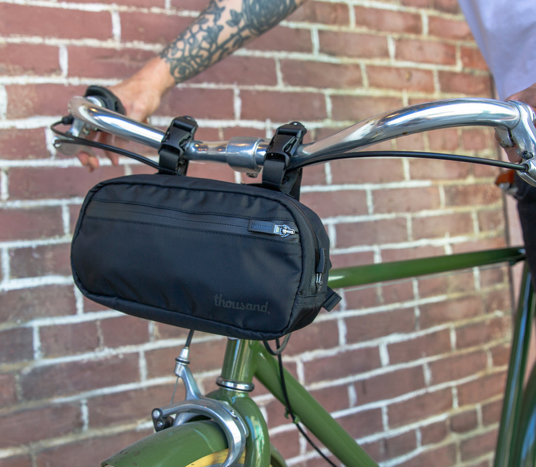 Crossbody Bag in schwarz am Fahrradlenker von grünem Fahrrad vor Mauer