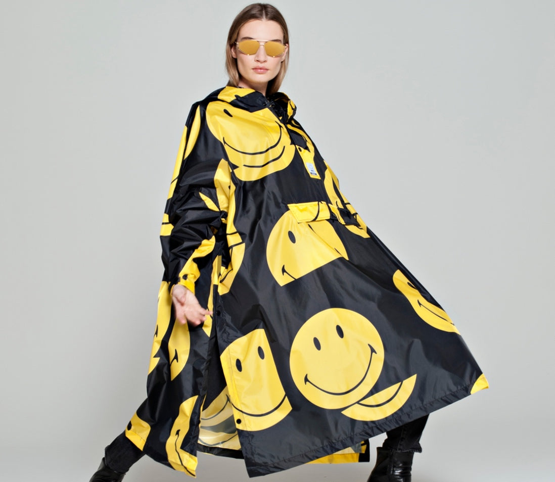 Rainkiss All Smiley Regenponcho mit gelben Smileys auf schwarzem Mantel Model mit Sonnenbrille
