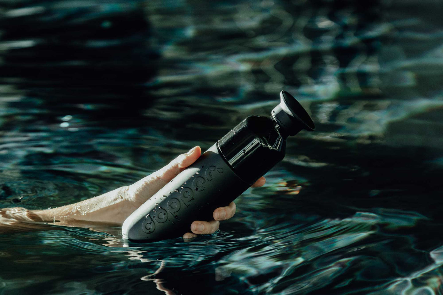Hand hält DOPPER Insulated Steel – Blazing Black Trickflasche beim Schwimmen im Wasser