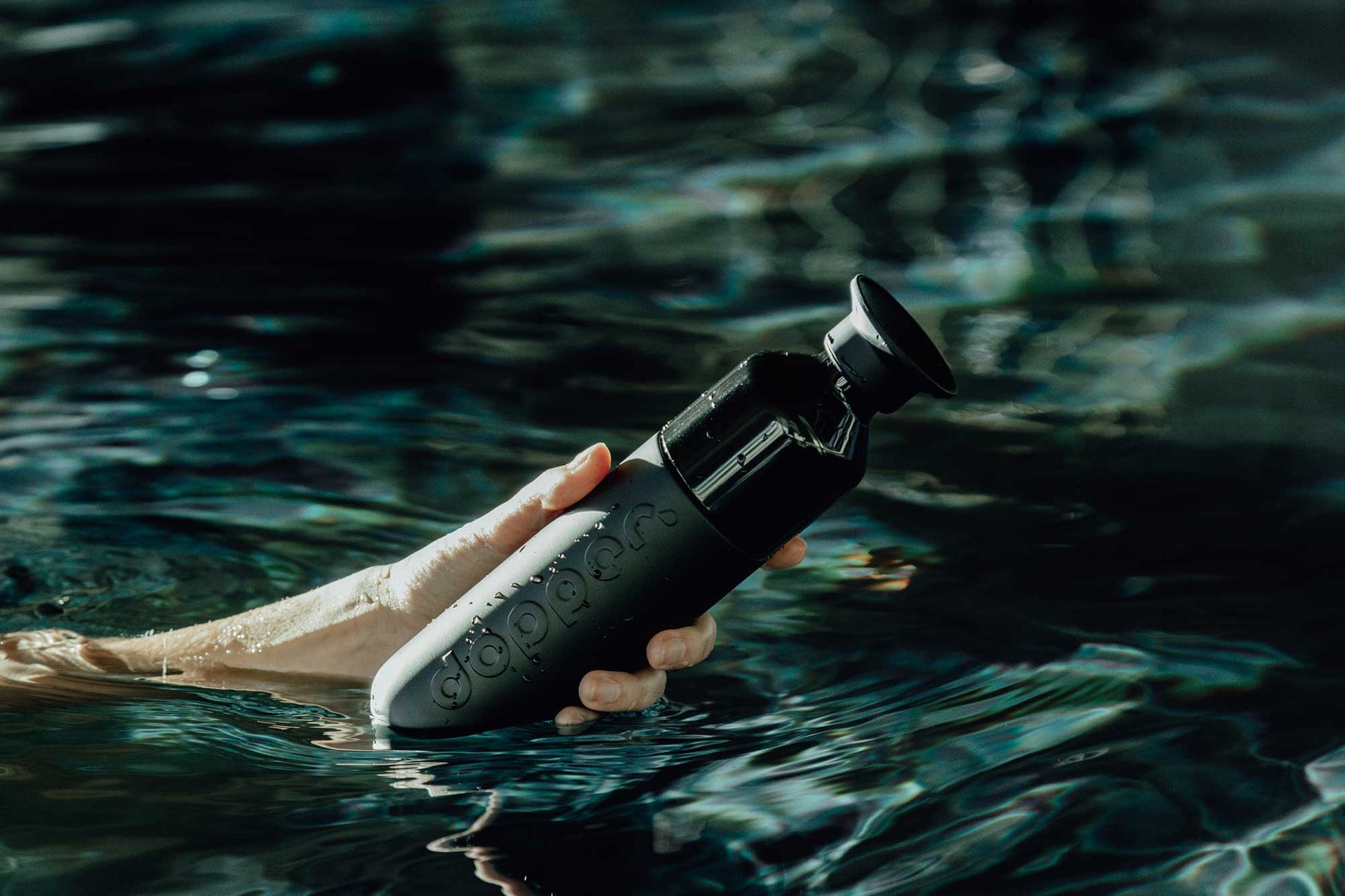Hand hält DOPPER Insulated Steel – Blazing Black Trickflasche beim Schwimmen im Wasser